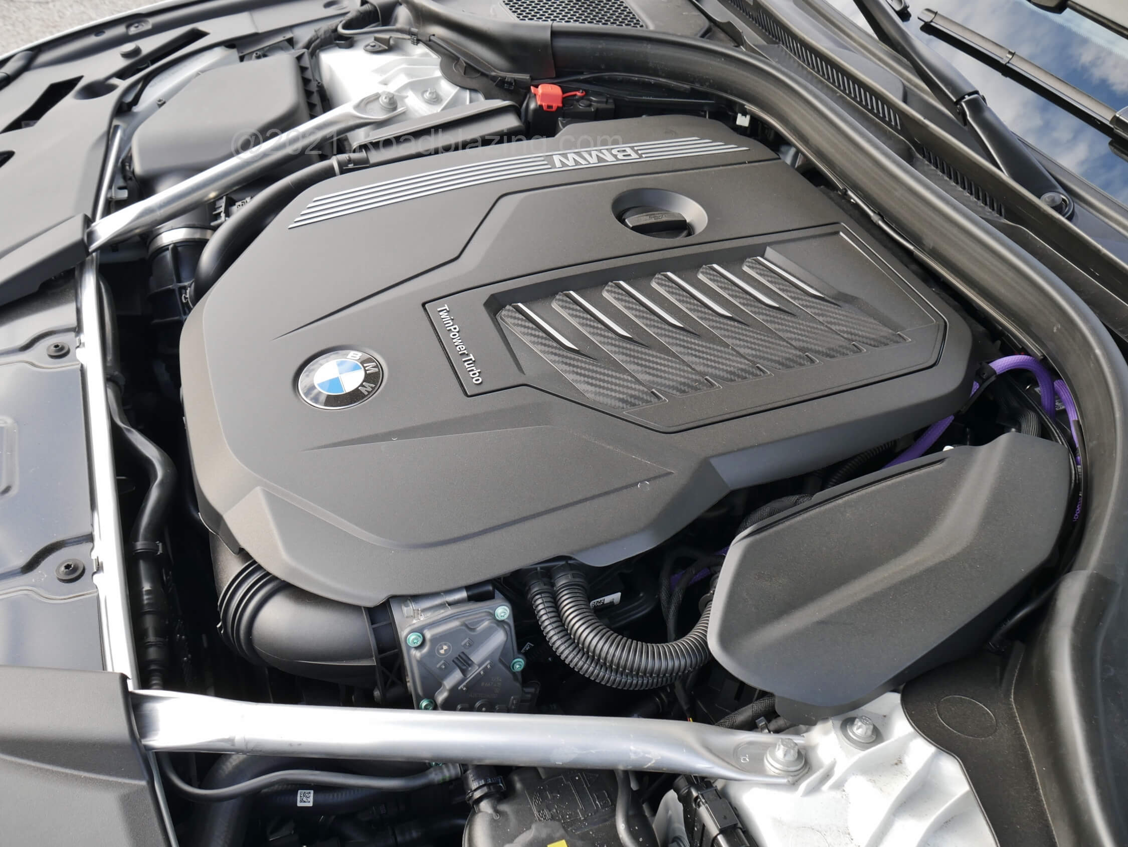 2021 BMW 540i xDrive: purple colored wiring harness on left side of engine intake cover betrays the 48 Volt mild hybrid regenerative generator motor which reduces parasitic losses